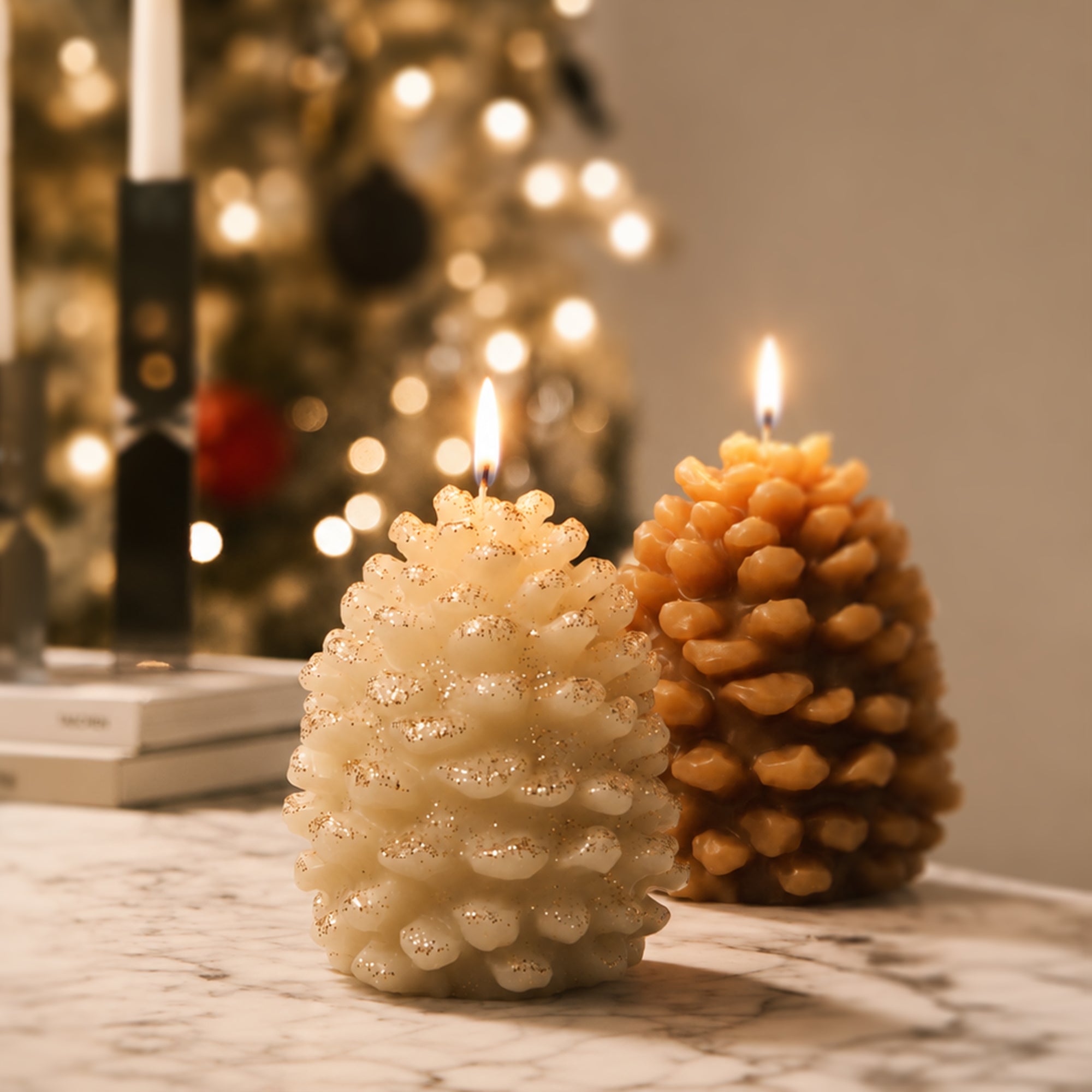 Two lit winter pinecone pillar candles in cream and caramel tones marble table Christmas bokeh background styling - Boowan Nicole