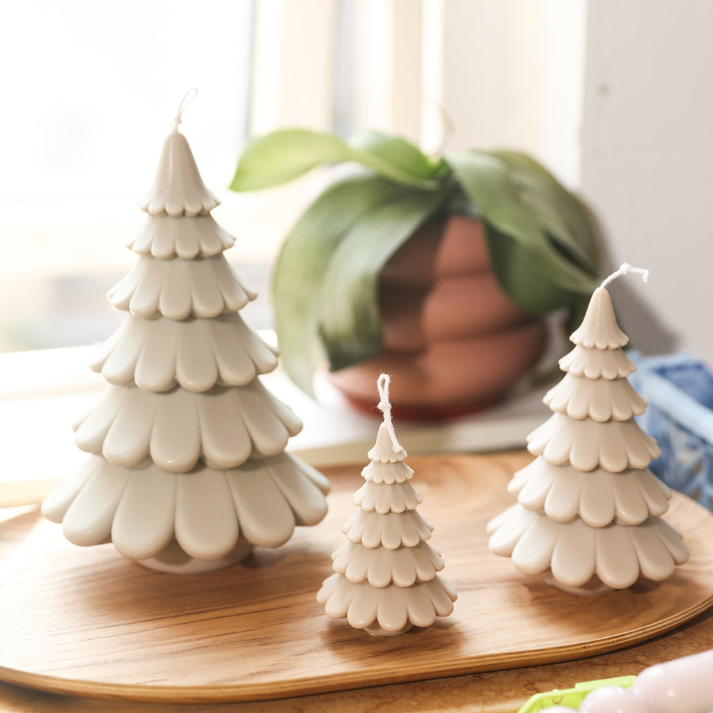 Three creamy white tiered Christmas tree candles are arranged in trays on the dining table, designed by Boowan Nicole.