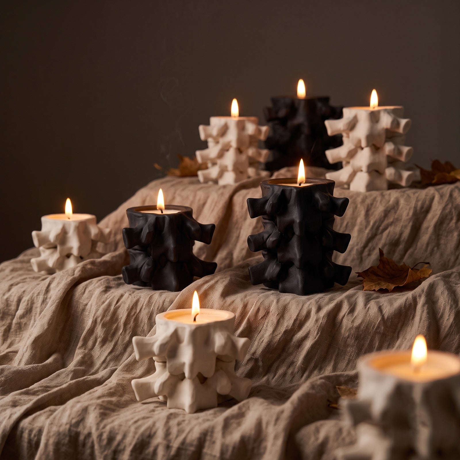 Multiple lit black and white Haunted Spine candle jars arranged on textured linen fabric - Boowan Nicole