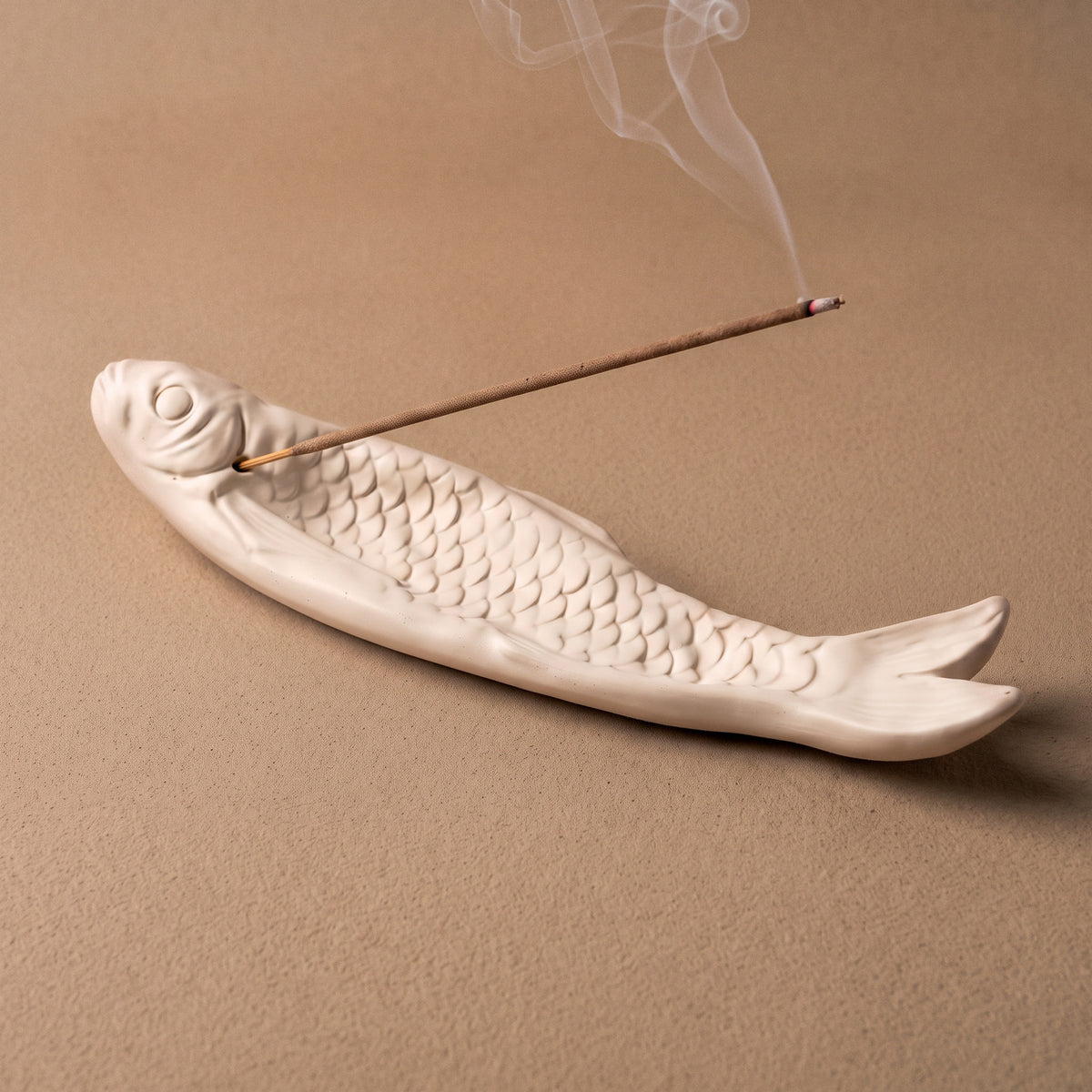 Fish-shaped incense holder with a burning incense stick on a warm-toned tabletop