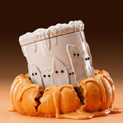 Ghostly cake shaped lidded candle jar with cute ghost silhouettes and dripping frosting design placed on pumpkin dessert for Halloween decor - Boowan Nicole