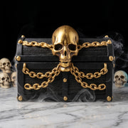 Closed pirate treasure chest candle jar decorated with golden skull and chains, surrounded by smoke and skull ornaments on marble surface - Boowan Nicole