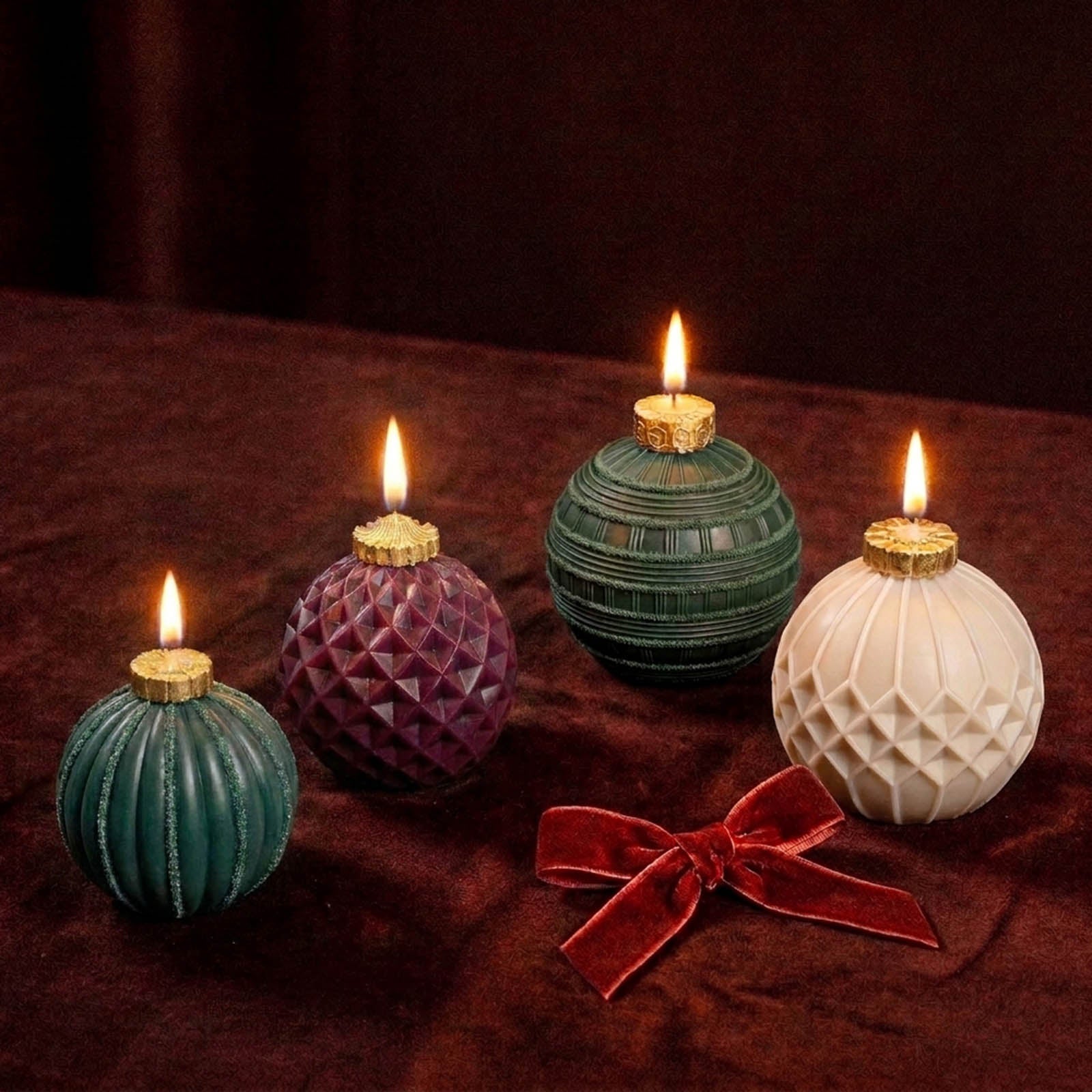 Four textured spherical wax candles with gold top caps and lit flames, arranged on a dark brown velvet surface with a red bow. The candles are in teal, purple, green, and cream colors.