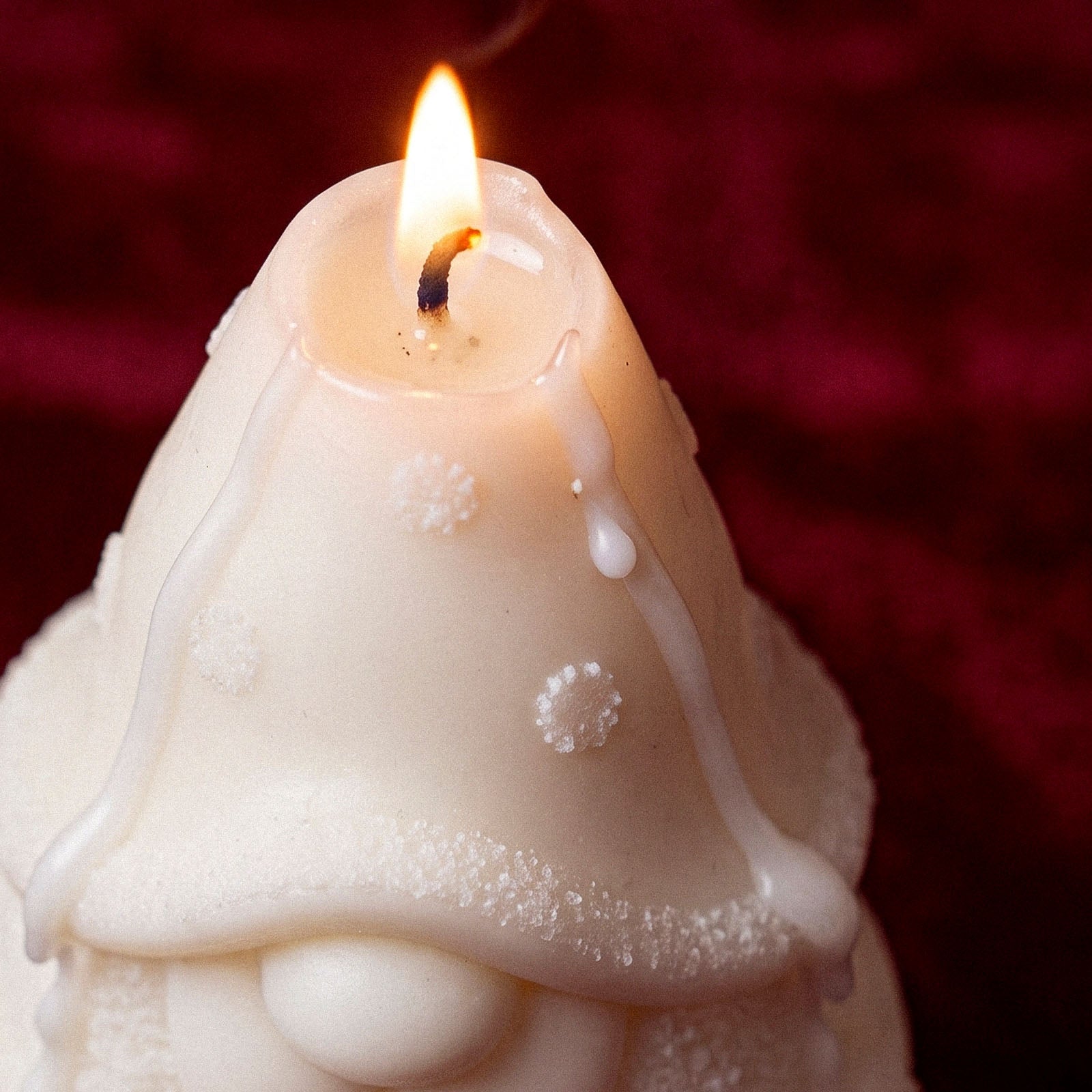 Close‑up of burning white gnome candle showing melting wax drip and hat snowflake textures - Boowan Nicole
