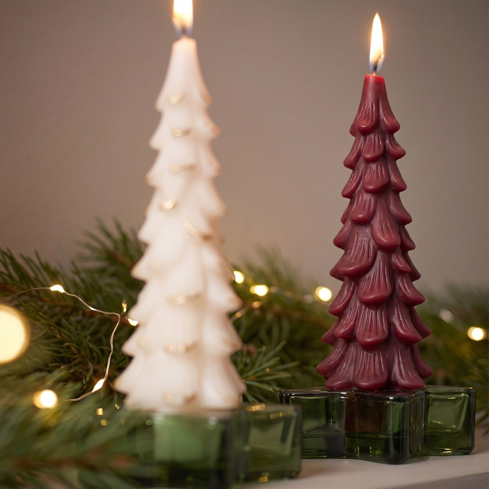 Close‑up view of burning white and burgundy winter pine taper candles with bokeh fairy lights background - Boowan Nicole