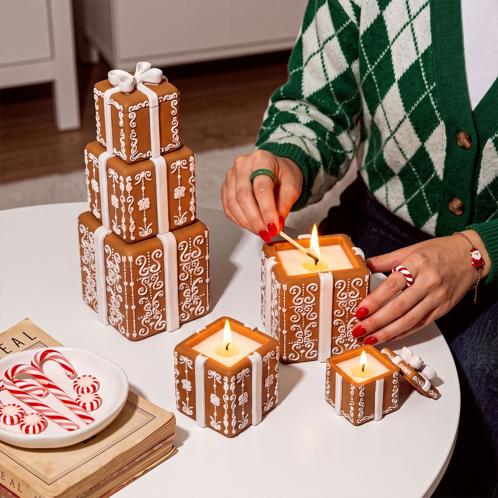 Gingerbread style stacked gift box candle jars being lit on white table Christmas decor - Boowan Nicole