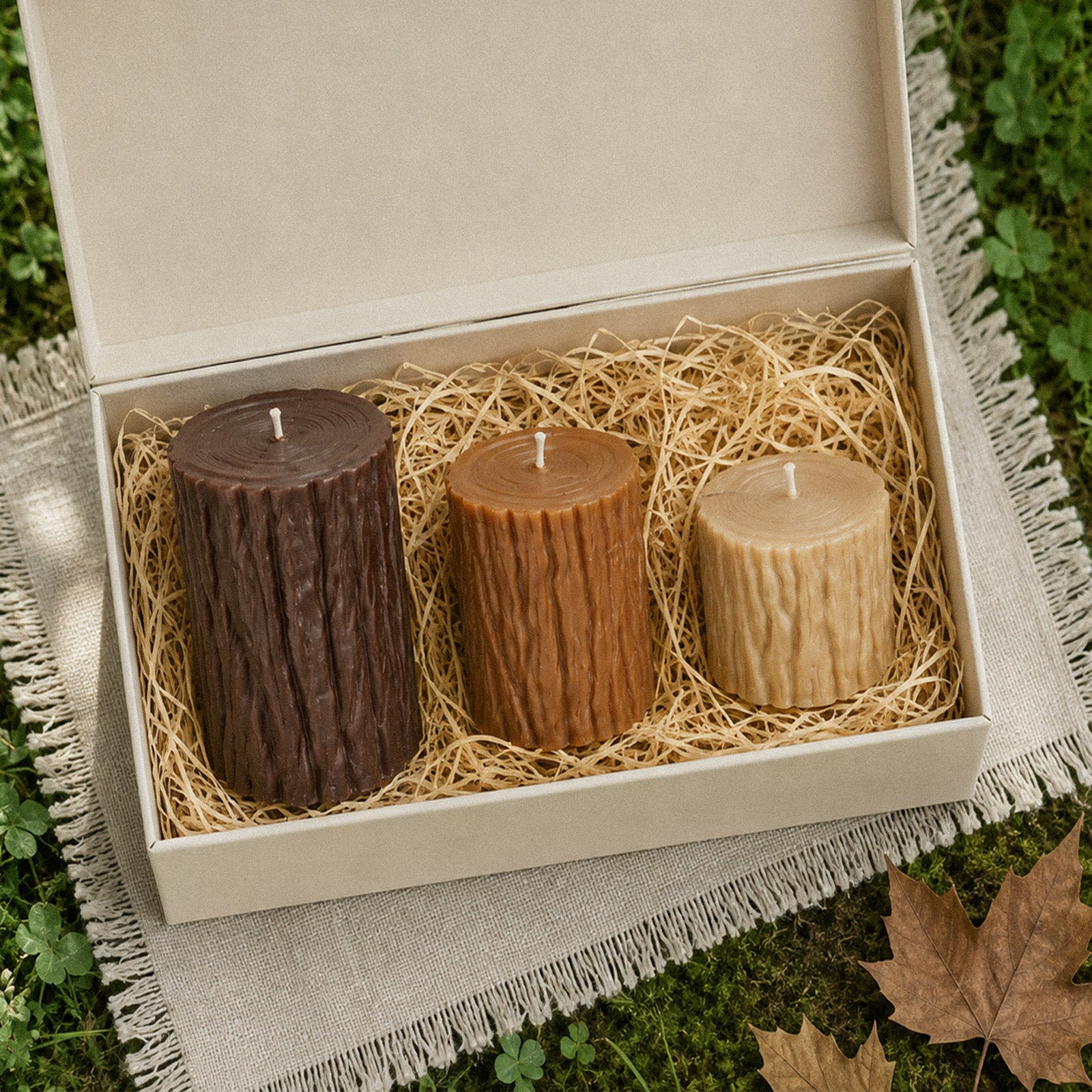 Gift set of three natural tree stump pillar candles arranged inside open gift box on linen over green grass - Boowan Nicole