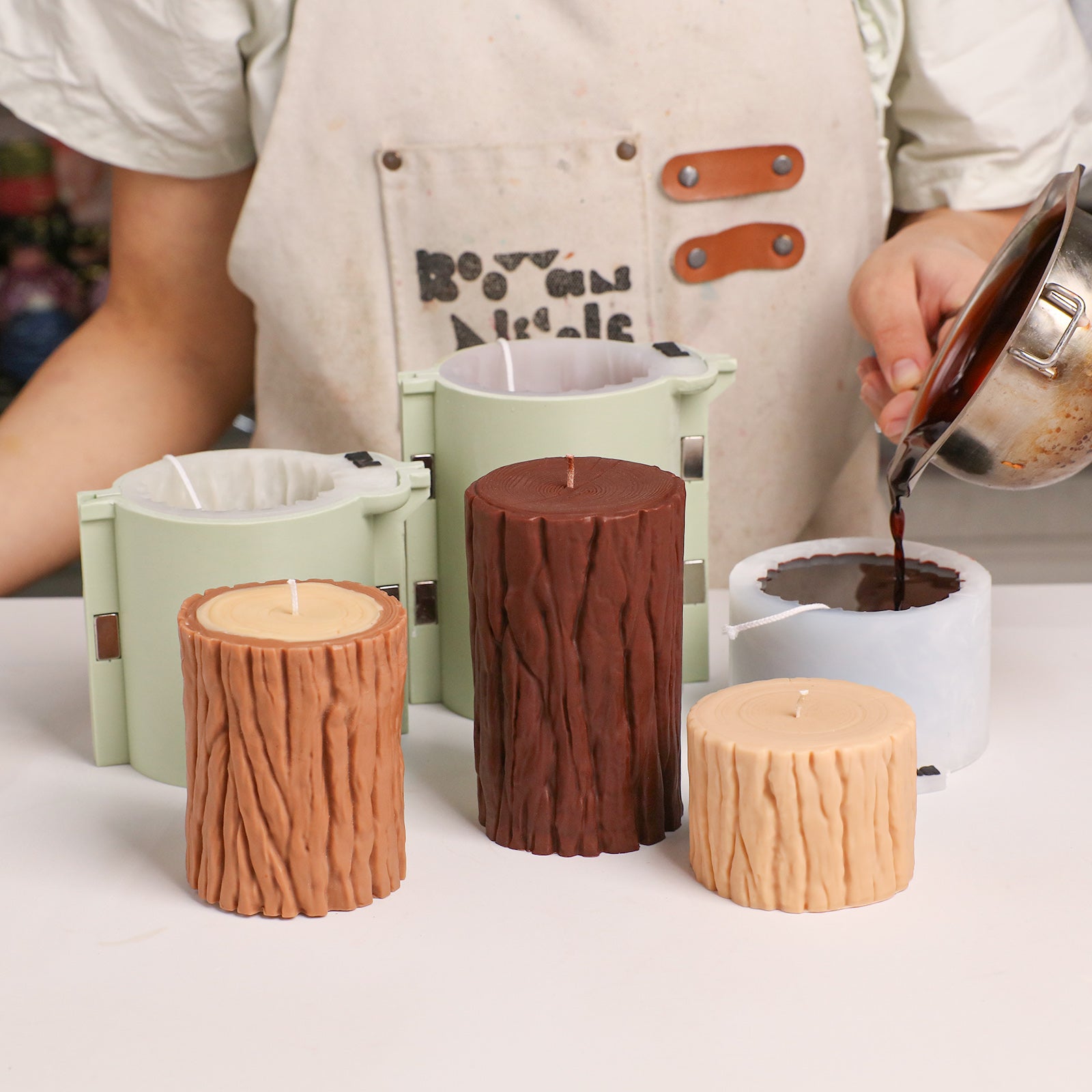 Pouring melted wax into multi-size tree stump silicone molds, finished bark-texture pillar candles displayed beside - Boowan Nicole