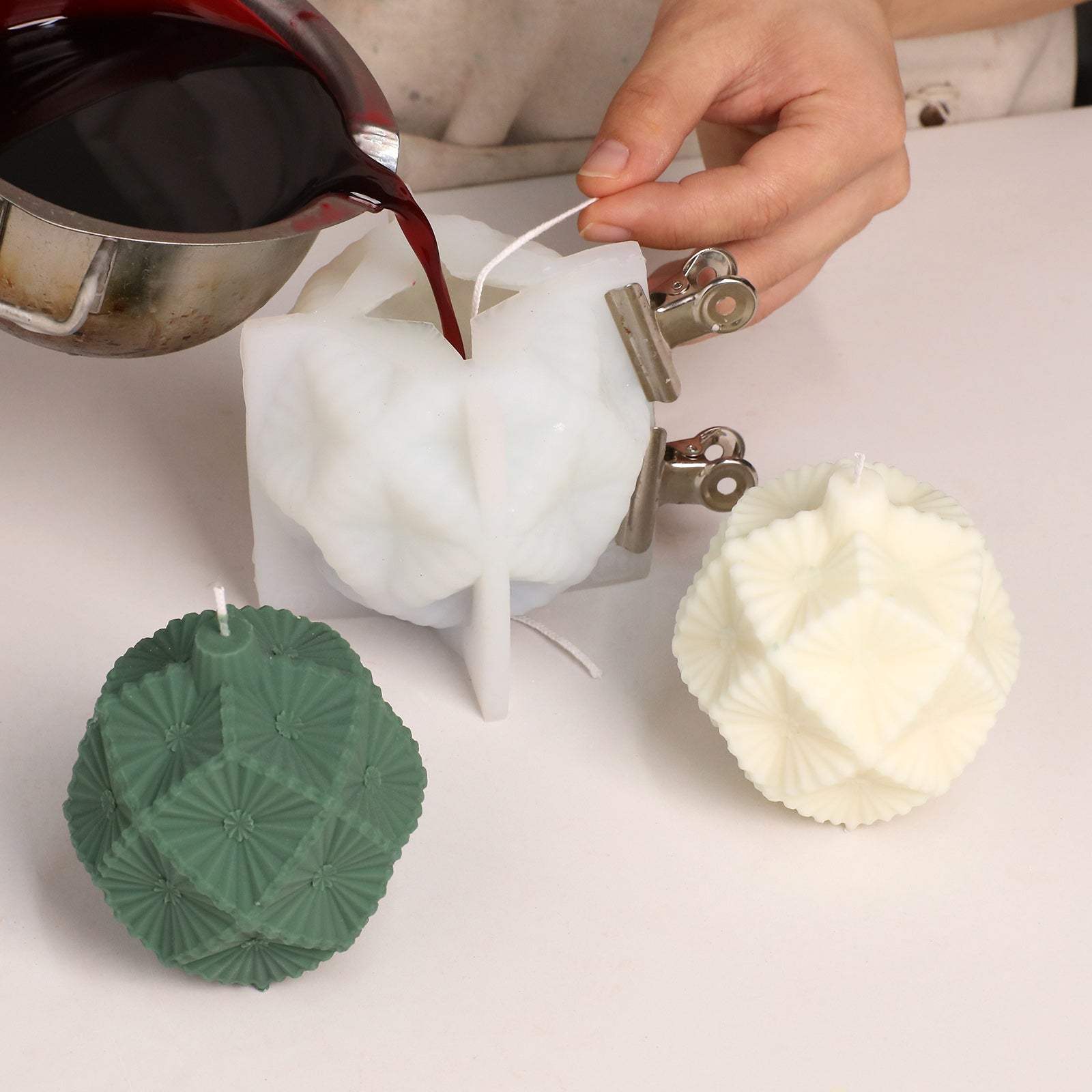 Pouring red melted wax into silicone mold for making geometric bauble‑shaped candle - Boowan Nicole