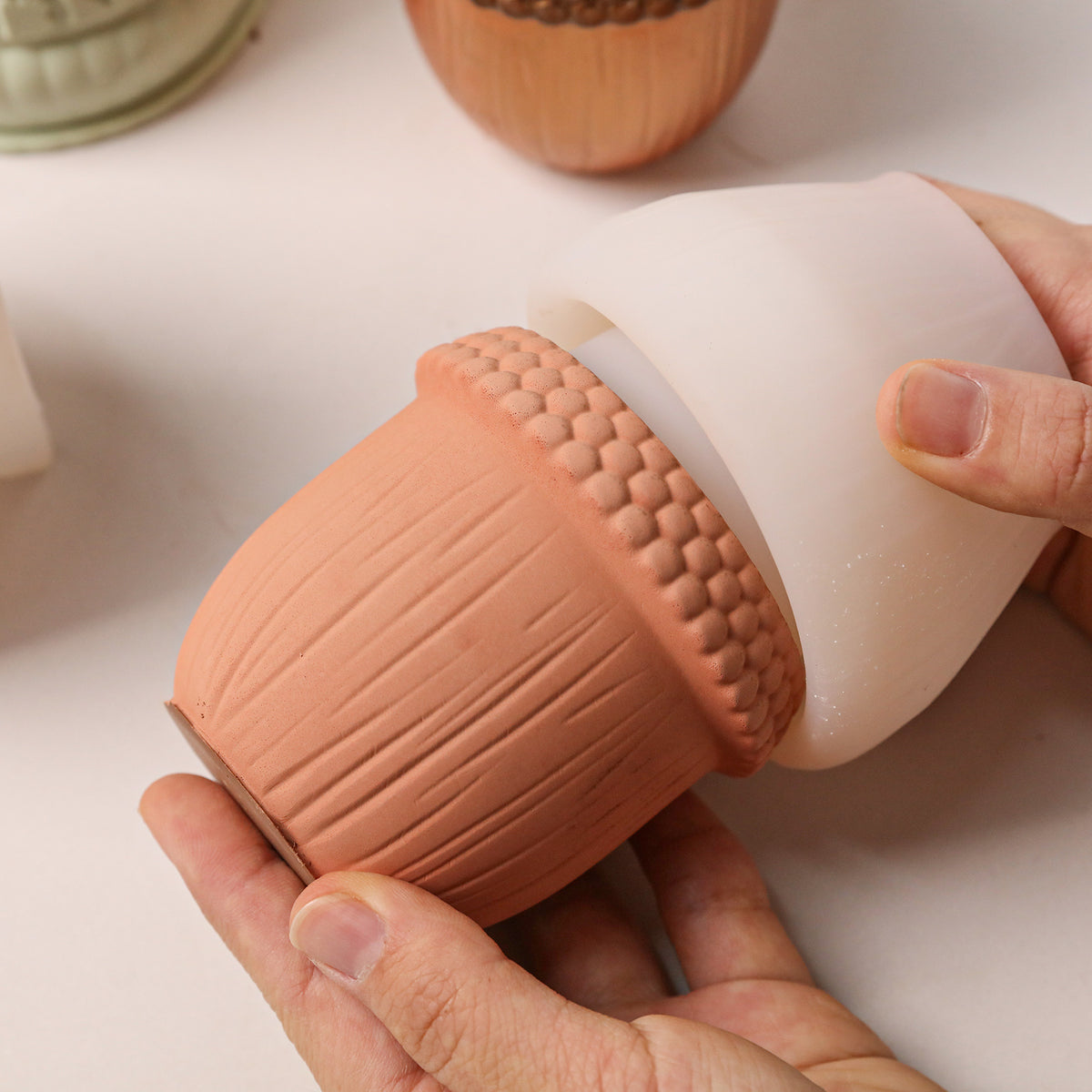 Hand removing cured acorn candle jar from white silicone mold, showing detailed acorn texture on finished piece - Boowan Nicole