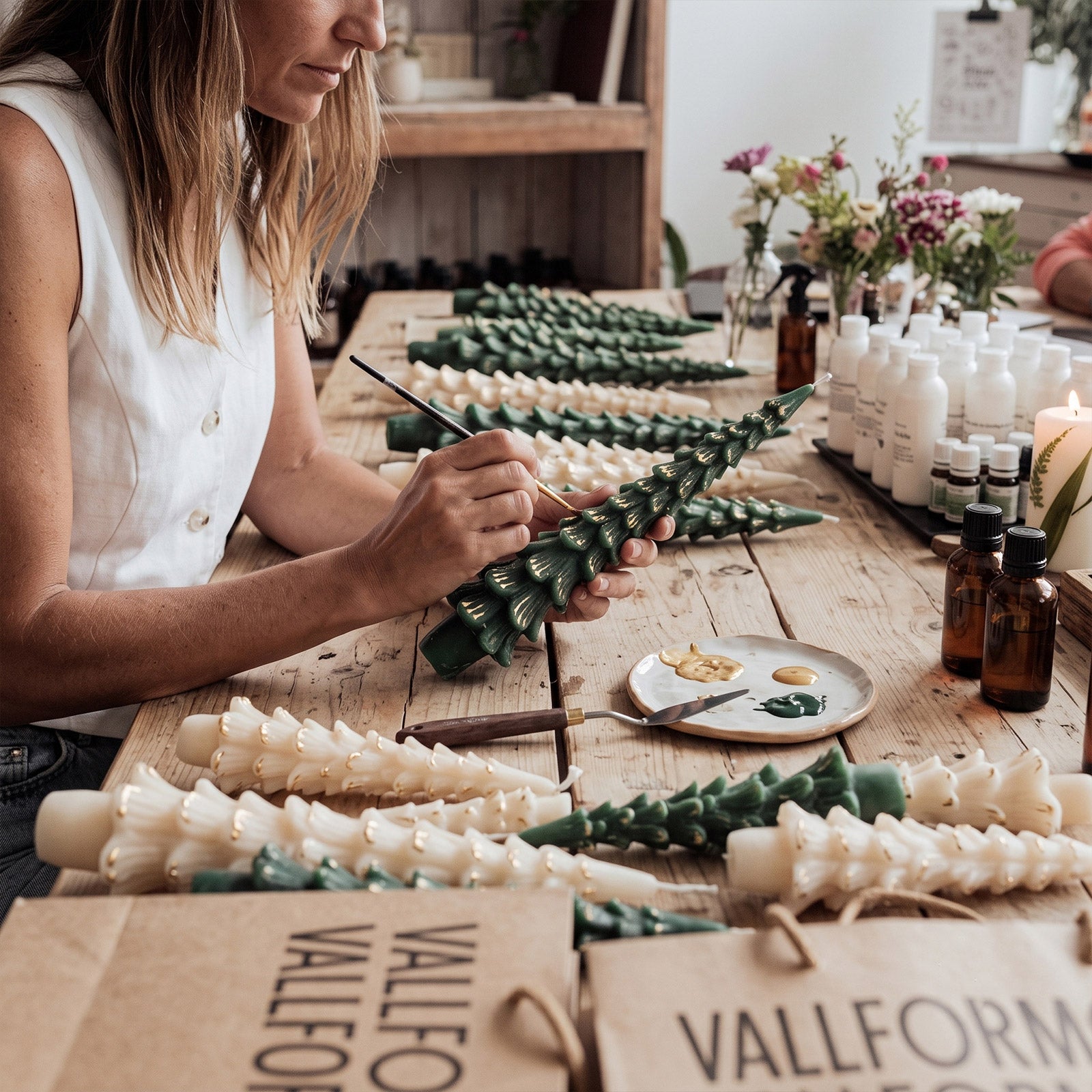 Crafter hand‑painting gold details on bulk handmade pine tree taper candles at workshop table - Boowan Nicole