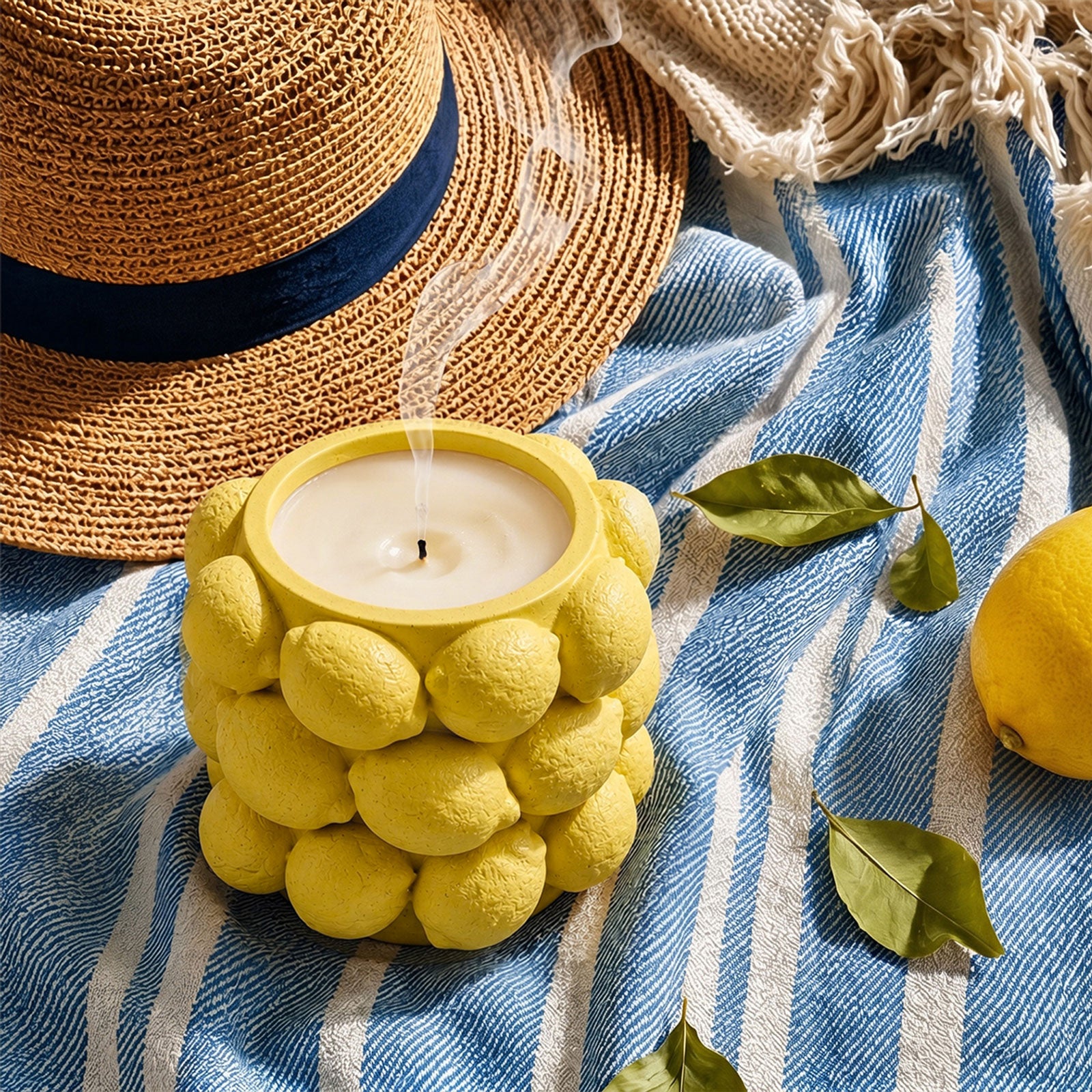 Burning yellow Lemon Drops candle jar styled with straw hat and fresh lemons for summer picnic scene - Boowan Nicole