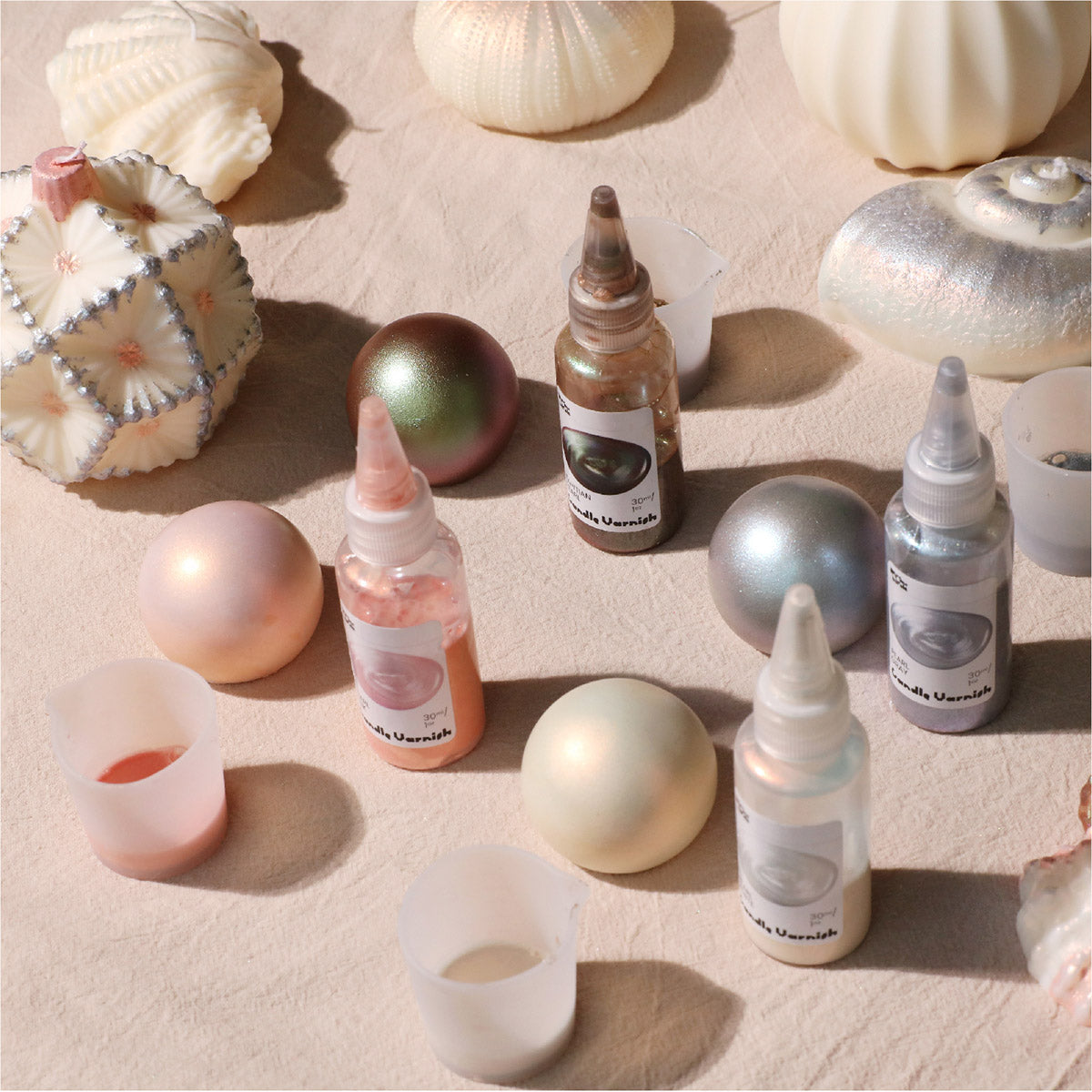 Various Shimmer Pearl Candle Varnish Bottles Next to Finished Pearlescent Handcrafted Candles - Boowan Nicole