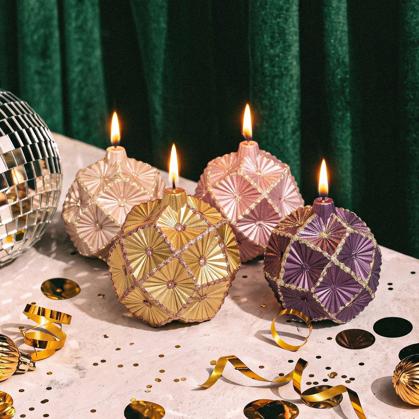 Group shot of assorted lit metallic‑finish geometric bauble Christmas candles on festive table setting - Boowan Nicole