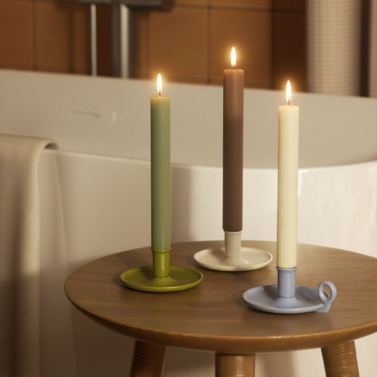 Three lit 9.3" classic taper candles—sage, taupe, and cream—in ceramic holders on a wooden stool by the bath - Boowan Nicole