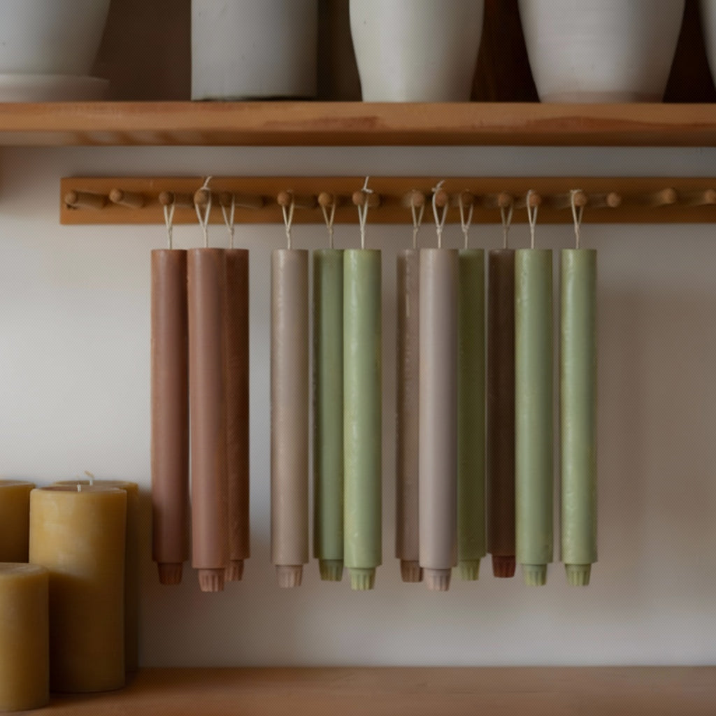 Pairs of 9.3" classic taper candles in sage, taupe, and clay tones curing on a wooden peg rail - Boowan Nicole