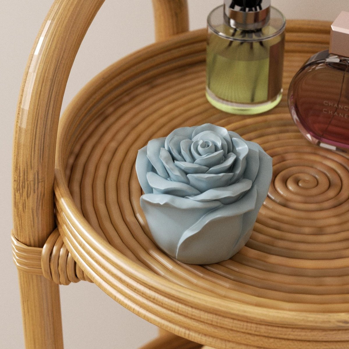 Light blue rose-shaped candle jar placed on a rattan tray table next to perfume bottles - Boowan Nicole
