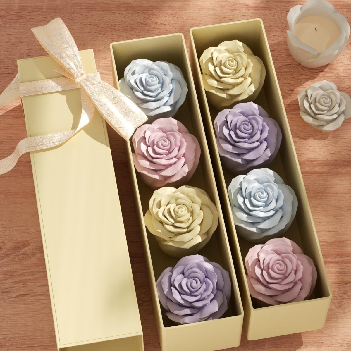 Two rows of pastel-colored rose-shaped candles neatly arranged in elegant long gift boxes with a satin ribbon, displayed on a wooden table - Boowan Nicole