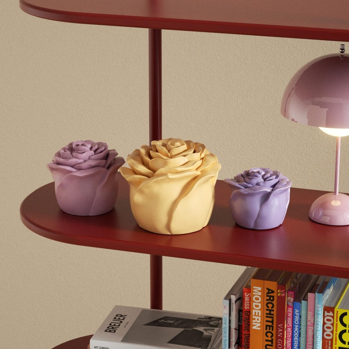 Three rose-shaped pastel candles in different sizes displayed on a red shelf with books and a lamp - Boowan Nicole