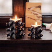 Black Haunted Spine candle jars with gold speckles lit on dark wooden windowsill - Boowan Nicole