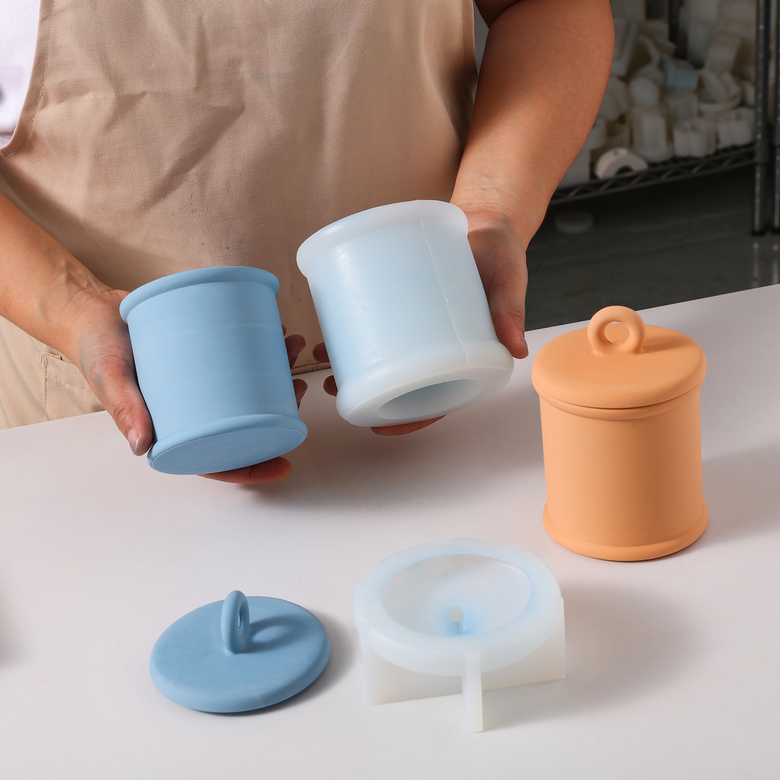 Hand showing blue Cylinder Short Candle Jar and silicone mold with ring lid on tabletop -Boowan Nicole