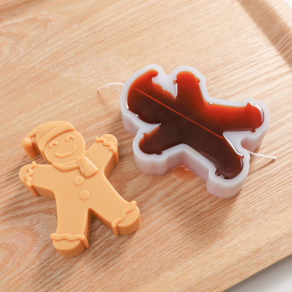 A gingerbread man candle is placed next to a white silicone mold filled with ginger wax, designed by Boowan Nciole.