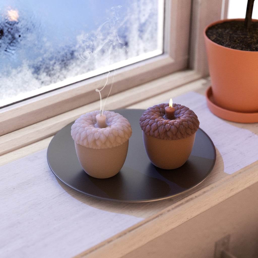 Two lit acorn-shaped candles are placed on a black tray by the window, creating a cozy and peaceful winter atmosphere-Boowan Nicole