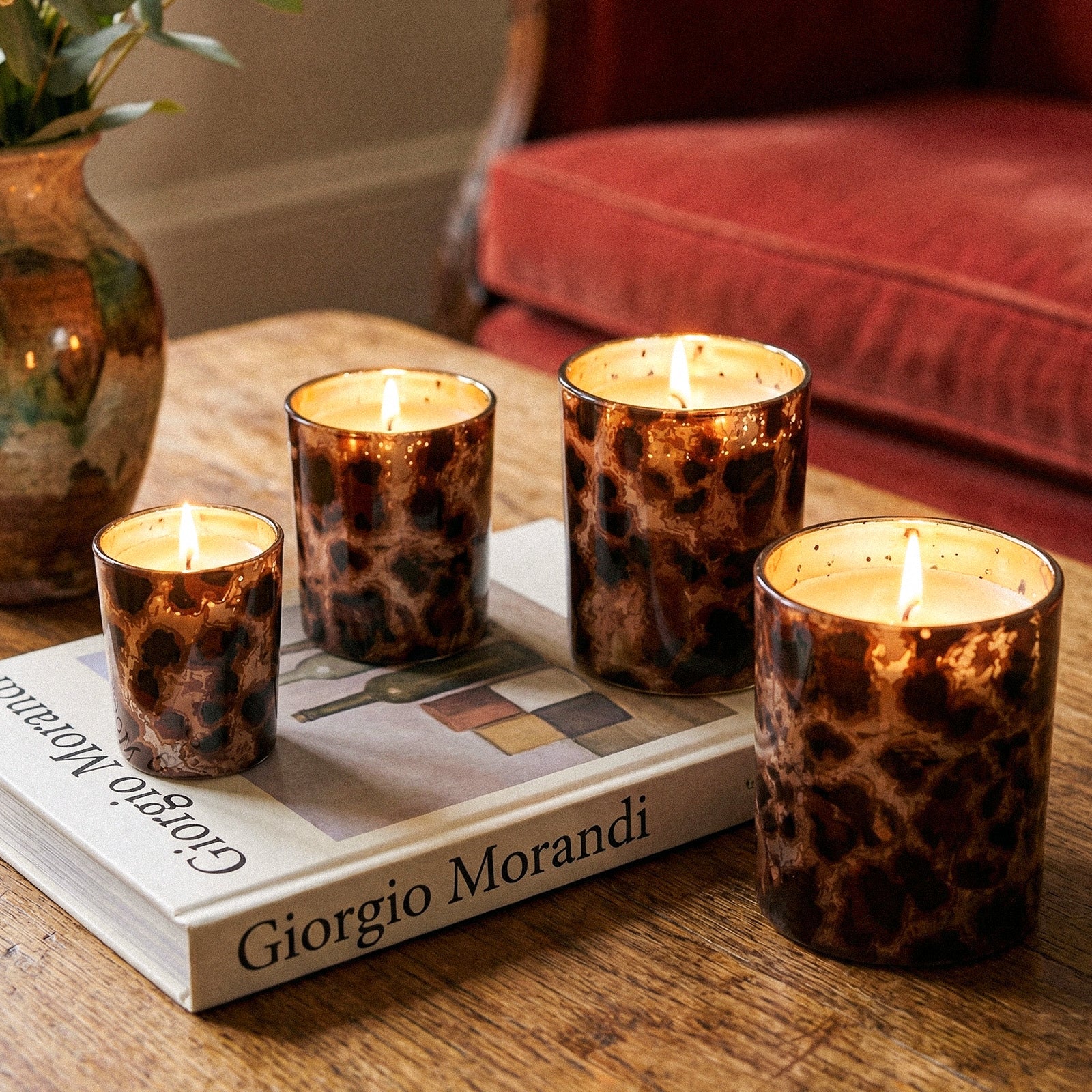 Four Burning Luxury Tortoise Print Candle Cups Arranged on Vintage Wooden Tabletop With Art Book - Boowan Nicole
