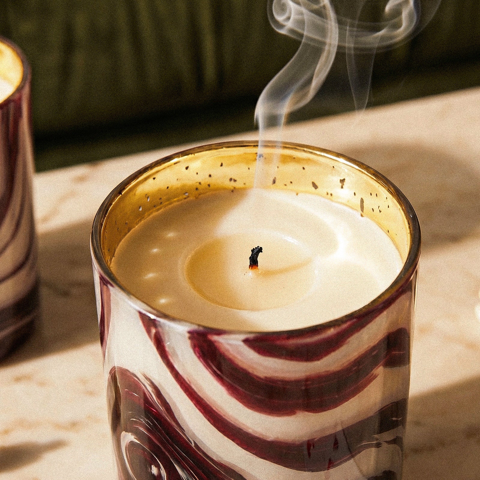 Two Burning Luxury Red White Marbled Candle Cups Arranged on Cream Marble Tabletop Beside Tufted Green Velvet Sofa - Boowan Nicole