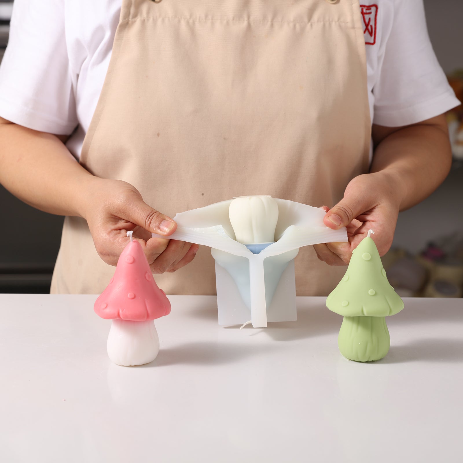 A hand holding a blue toad cap mushroom-shaped candle displayed in a white silicone mold, designed by Boowan Nicole.