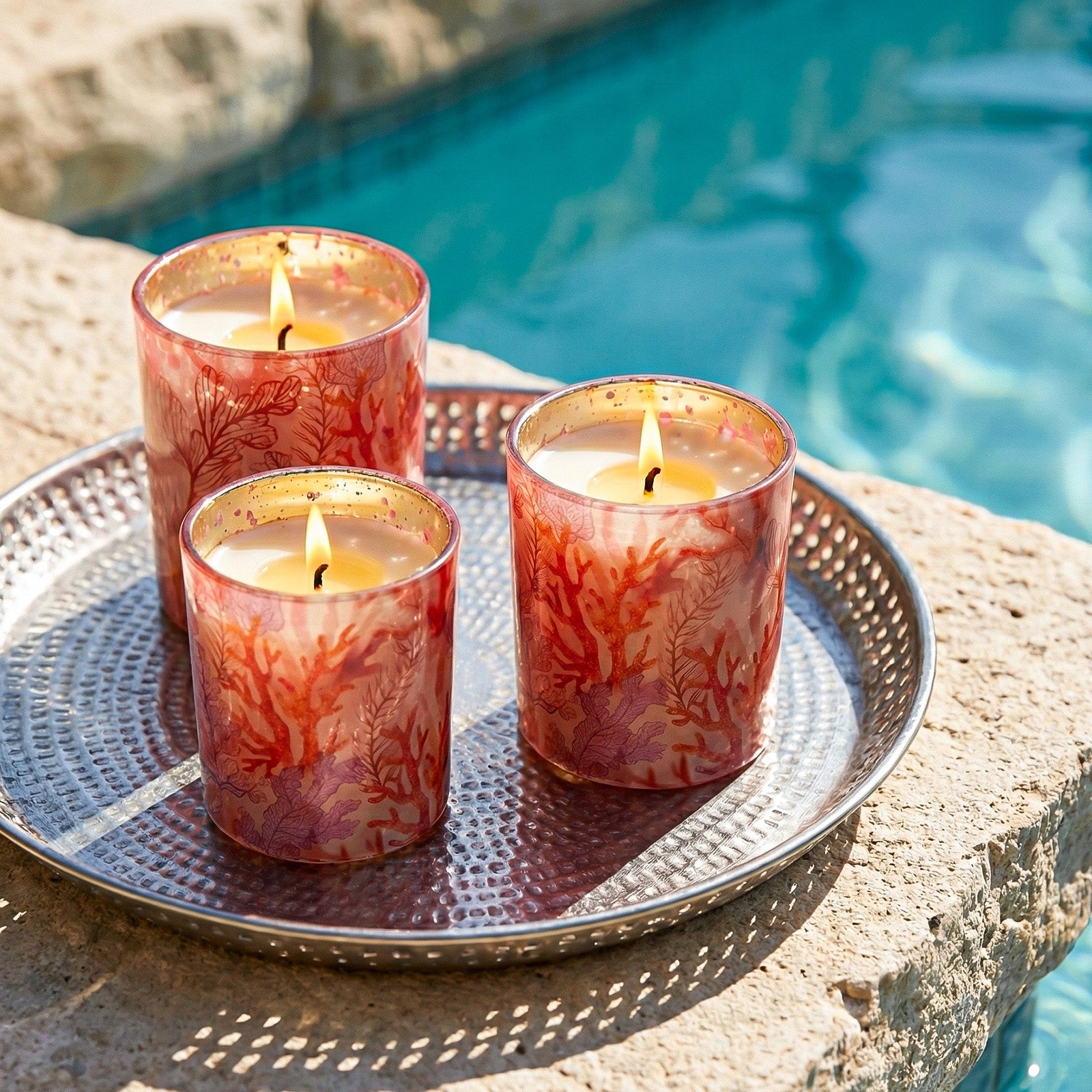 Three Lit Red Coral Candle Vessels Laid on Hammered Metal Tray Beside Outdoor Pool - Boowan Nicole