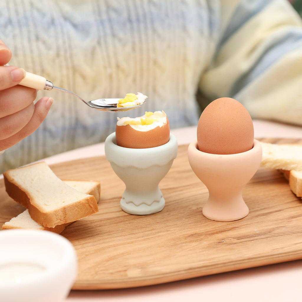 An open egg in one egg cup, with a spoon scooping out the egg.