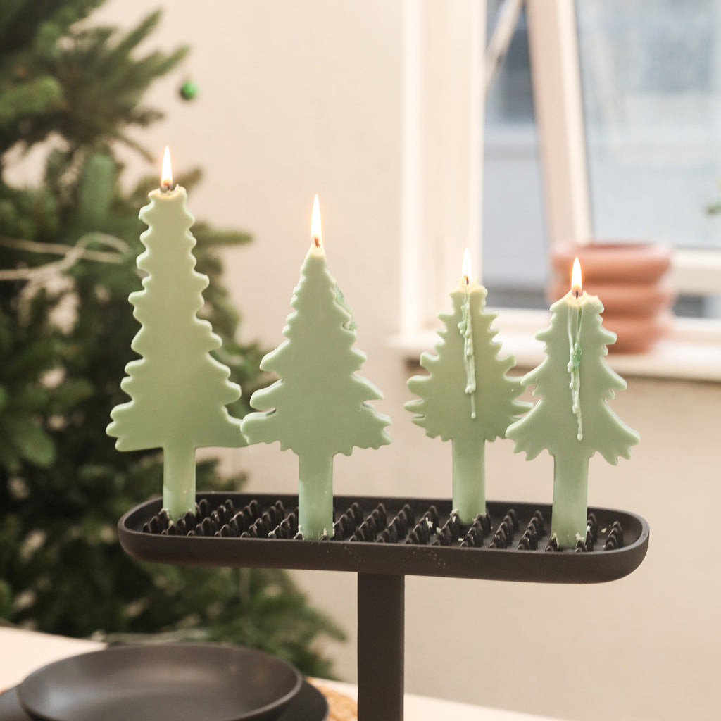 Four taper candles in the shape of Christmas trees placed on the dining table candlesticks.