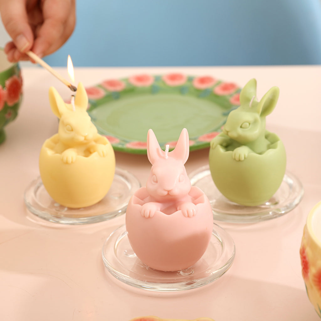 Three Easter Bunny candles are placed in a glass tray, one of which is being lit.