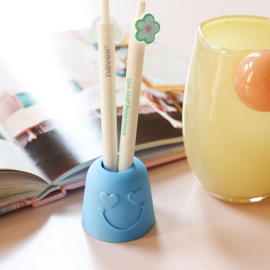 The Pen & Toothbrush Holder decorated with blue love eyes holds a pen inserted in it -Boowan Nicole
