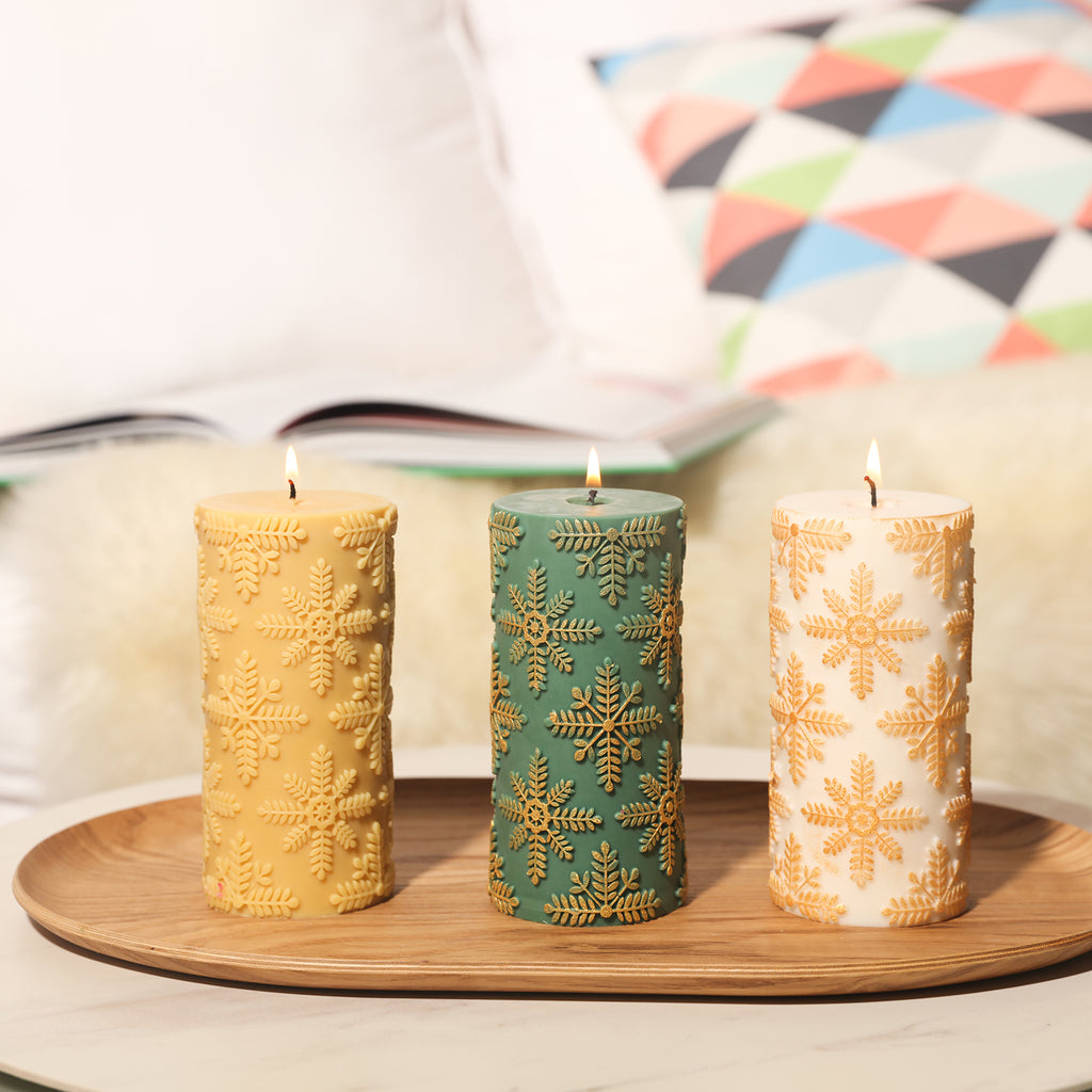 Green, yellow, and white long cylindrical snowflake relief candles are placed in trays on the table, adding to the festive atmosphere.