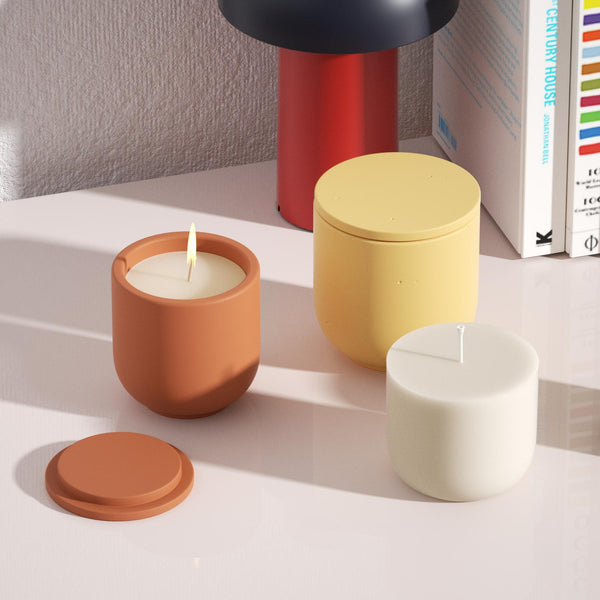 Candles in small orange candle jars are being lit next to candle refills and large yellow candle jars with flat lids