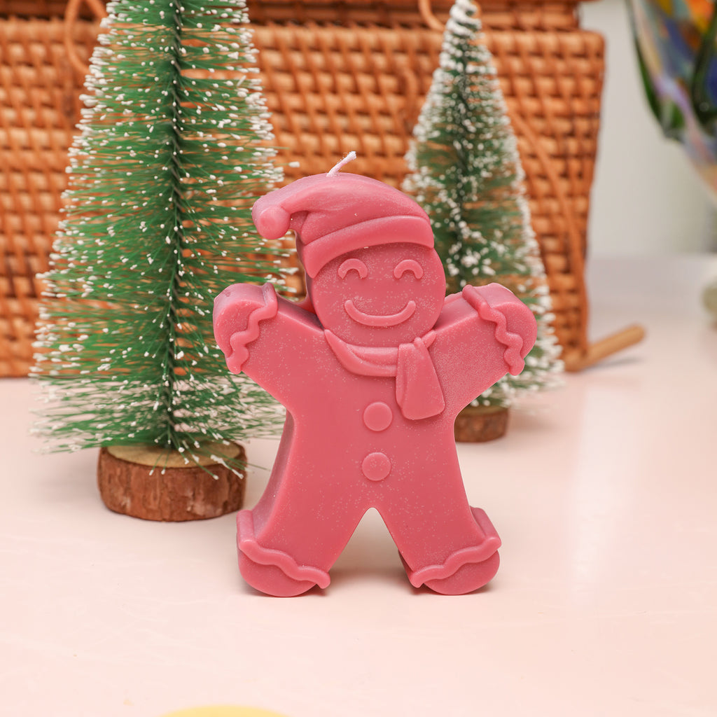 Red Gingerbread Baby candle is placed on the table with a Christmas tree decoration behind it - Boowan Nicole