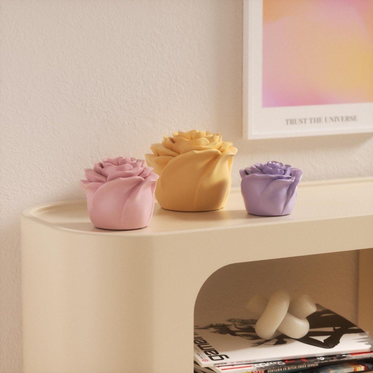 Three pastel rose-shaped candles in pink, yellow, and purple displayed on a light-colored shelf - Boowan Nicole