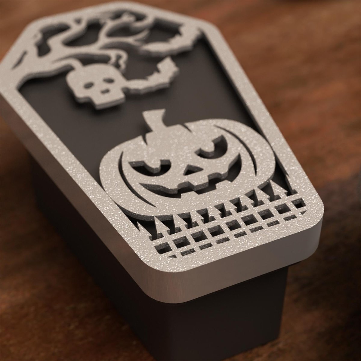 Close-up of a black coffin-shaped Halloween candle with glittery silver lid featuring a carved jack-o'-lantern and skull tree design - Boowan Nicole