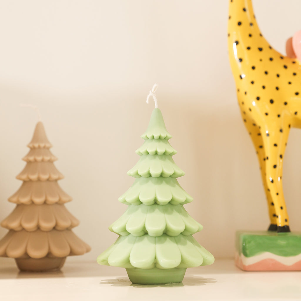 Green tiered Christmas tree candles sit on a shelf, designed by Boowan Nicole.