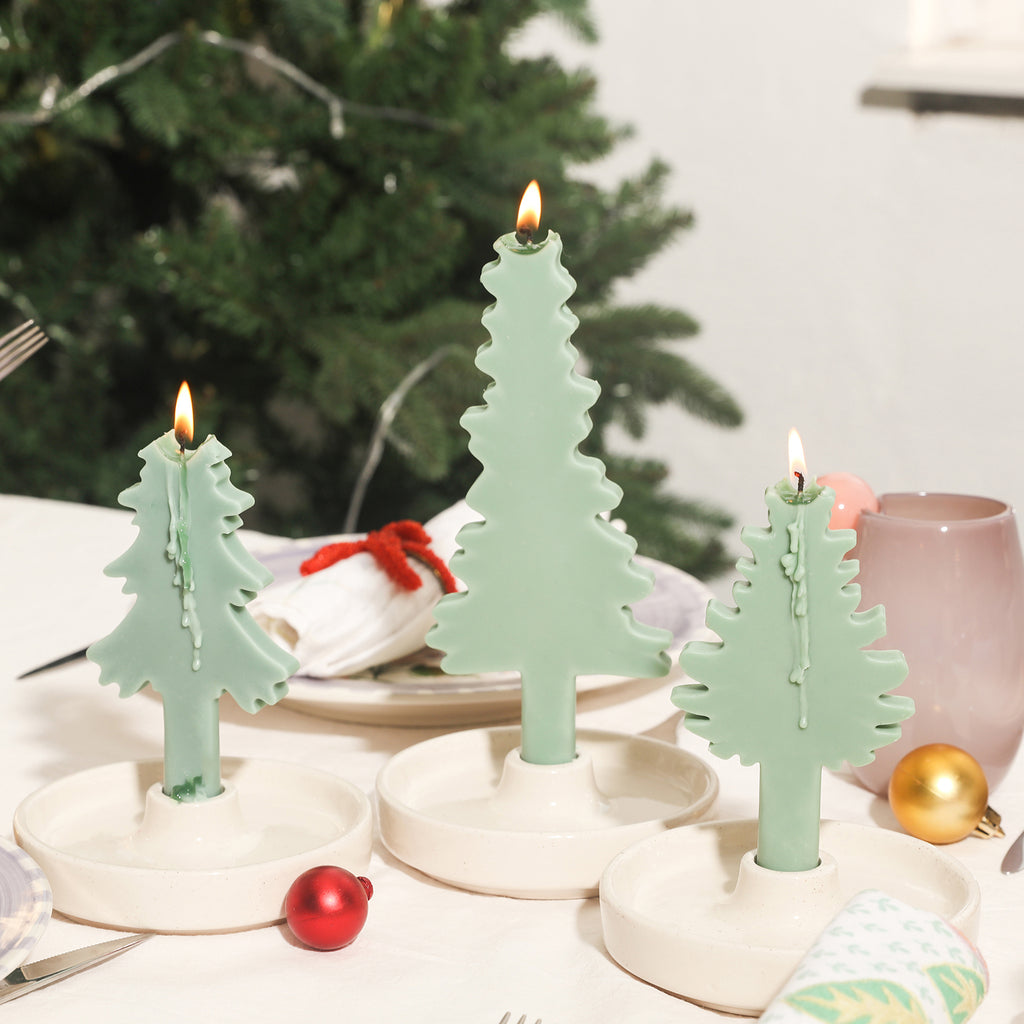 The green Christmas evergreen tree silhouette candle is burning, and the wax liquid slowly remains, adding to the festive atmosphere.