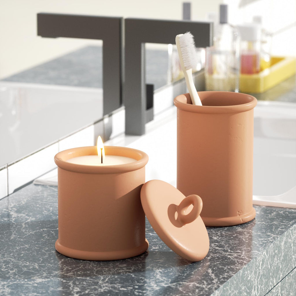 The candle in the brown Cylinder Short Candle Jar is burning slowly, and a toothbrush is placed in the long candle jar next to it -Boowan Nicole