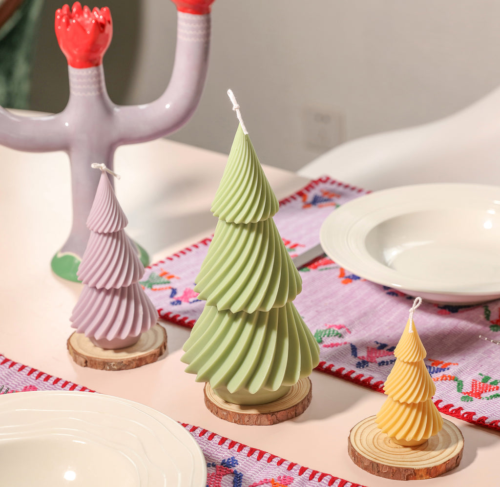 On the wooden tray on the dining table are placed large, medium and small green, purple and yellow evergreen Christmas tree candles - Boowan Nicole.