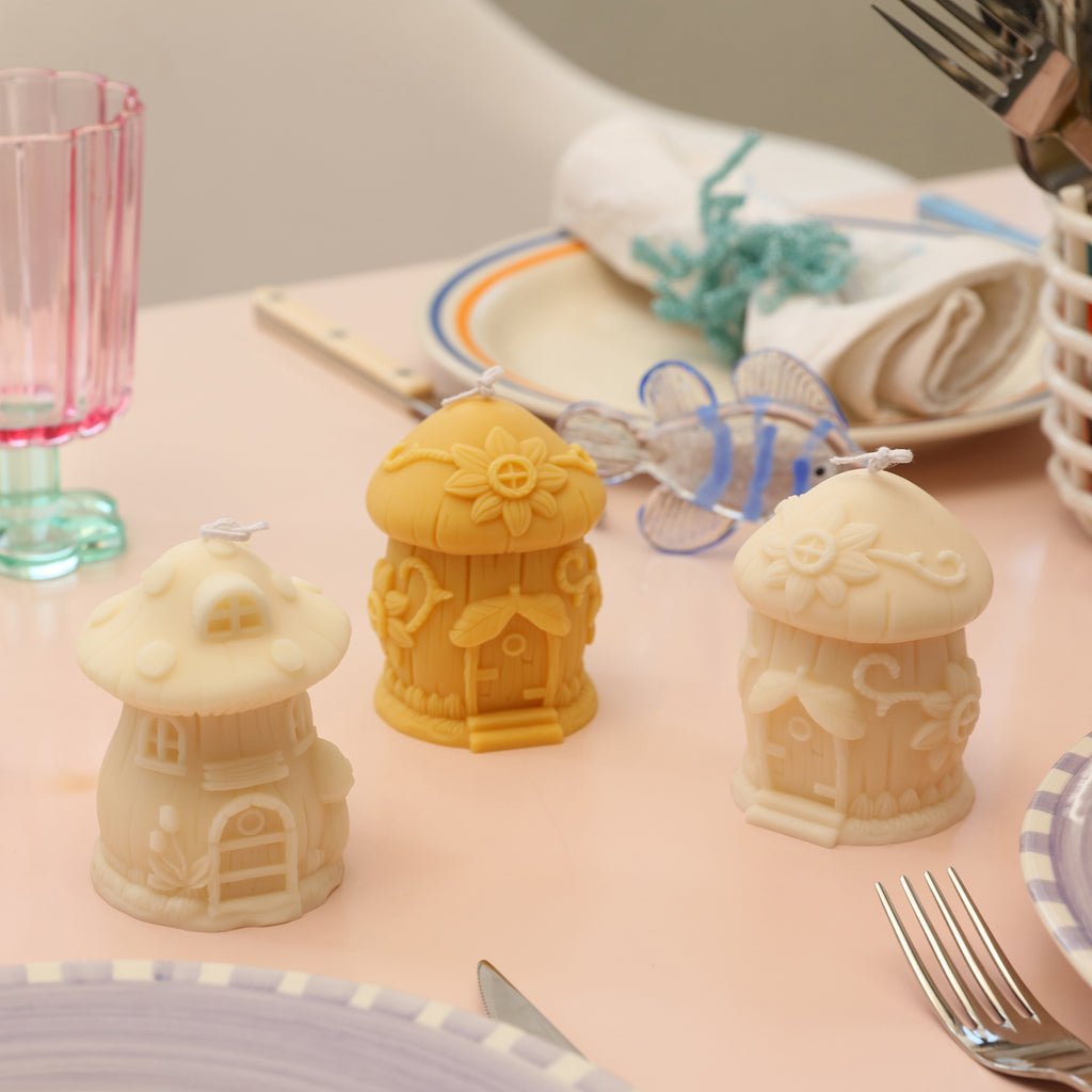 Three yellow mushroom house candles of different shapes are placed on the dining table, designed by Boowan Nicole.