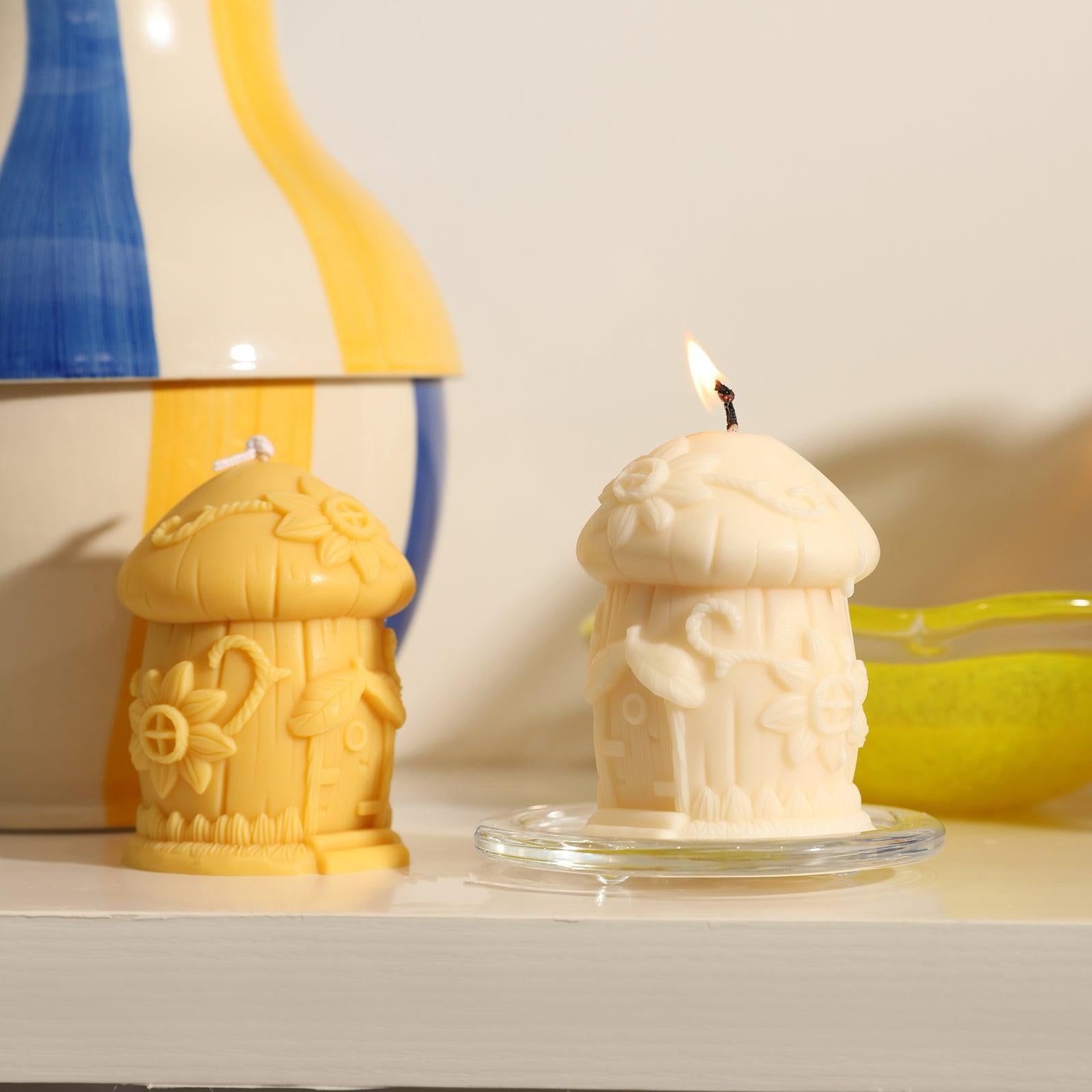 White Miniature Mushroom House Candle on a crystal tray is burning slowly, next to a yellow Miniature Mushroom House Candle -Boowan Nicole