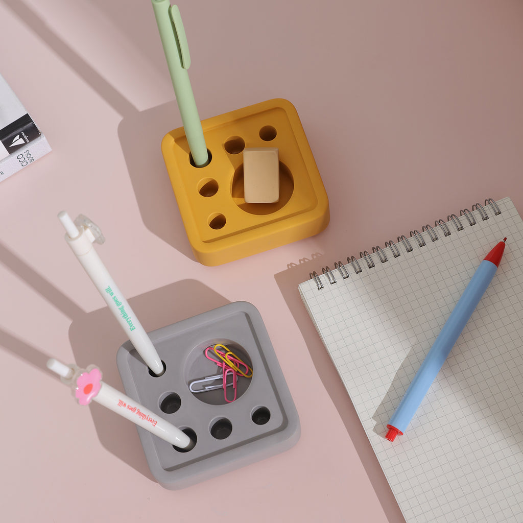 The yellow and gray Square Multi-Functional Stationery Support is placed on the desk with a notebook next to it - Boowan Nicole
