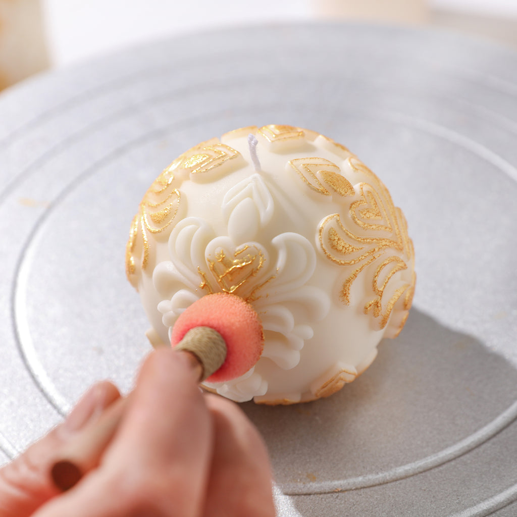 Creative touch with gold mica powder on a white sphere patterned relief candle.