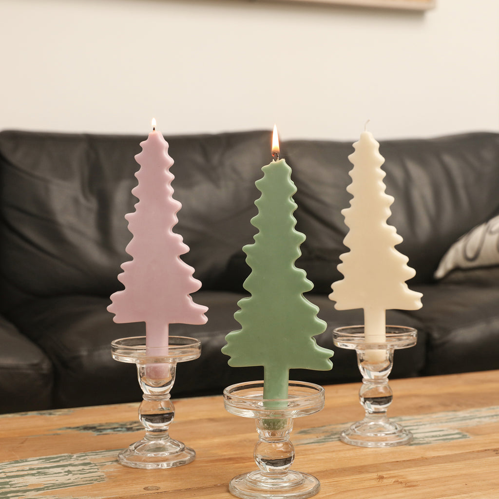 White, pink and green Christmas evergreen tree silhouette candles are burning slowly in crystal candle holders on the table.