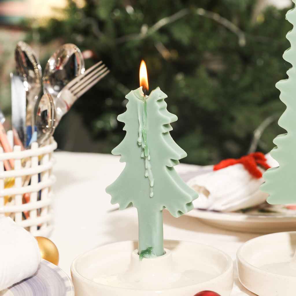 A green Christmas tree-shaped candle placed on a candle holder is burning slowly.